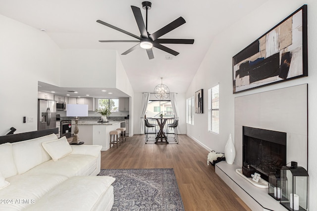 living room with a fireplace, ceiling fan with notable chandelier, high vaulted ceiling, and dark hardwood / wood-style flooring