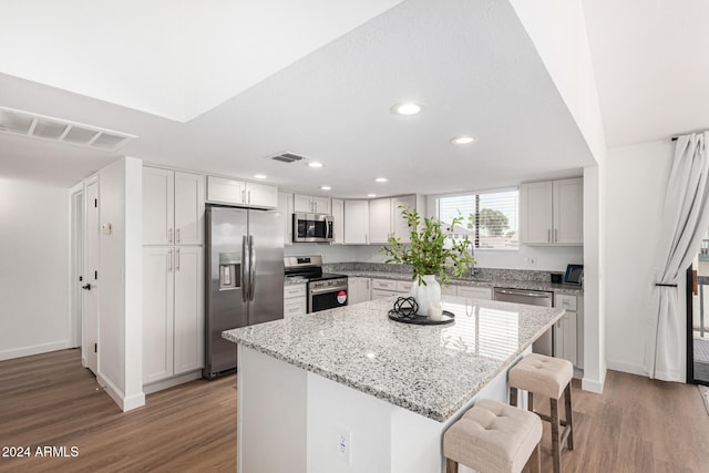 kitchen with wood-type flooring, light stone counters, stainless steel appliances, a kitchen island, and a breakfast bar