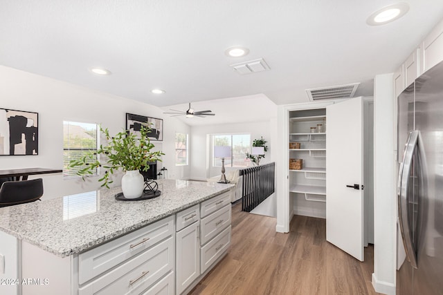 kitchen with white cabinets, light hardwood / wood-style flooring, light stone counters, and stainless steel refrigerator