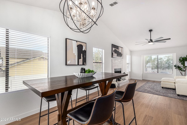 dining space with hardwood / wood-style floors, ceiling fan, a tiled fireplace, and lofted ceiling