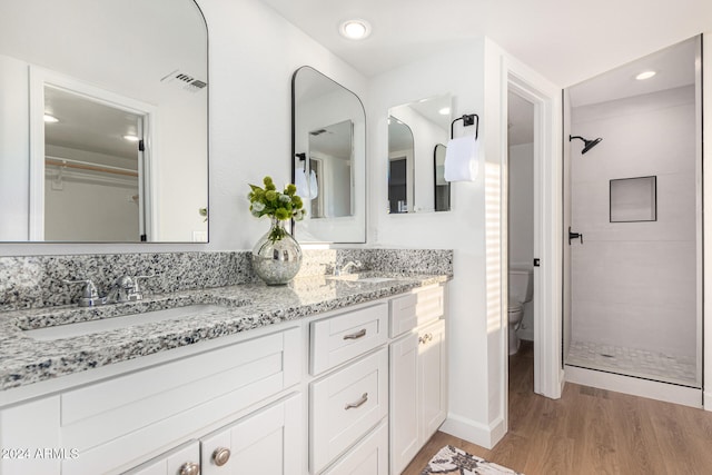 bathroom with hardwood / wood-style flooring, vanity, toilet, and tiled shower