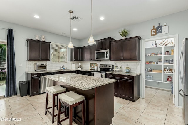 kitchen featuring visible vents, dark brown cabinets, appliances with stainless steel finishes, a center island, and pendant lighting