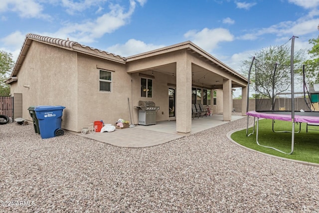 rear view of house featuring a trampoline, a tile roof, stucco siding, a patio area, and a fenced backyard