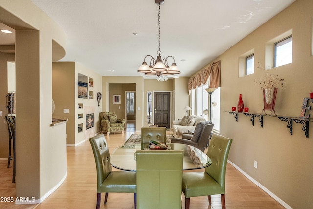 dining space with a fireplace, a notable chandelier, light hardwood / wood-style flooring, and plenty of natural light