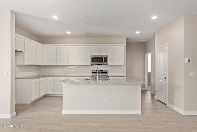 kitchen featuring white cabinetry, stainless steel appliances, an island with sink, and light stone counters