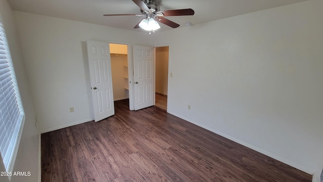 unfurnished bedroom with wood finished floors, baseboards, a spacious closet, a closet, and a ceiling fan