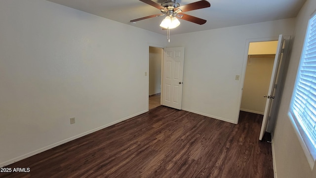unfurnished bedroom with dark wood-style floors, a walk in closet, baseboards, and a closet