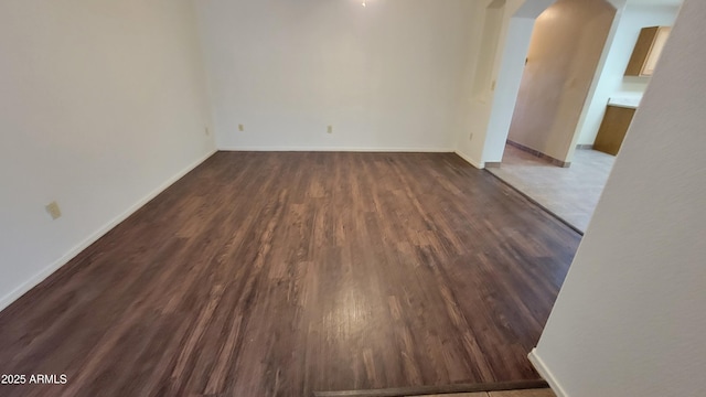 unfurnished room with arched walkways, dark wood-type flooring, and baseboards