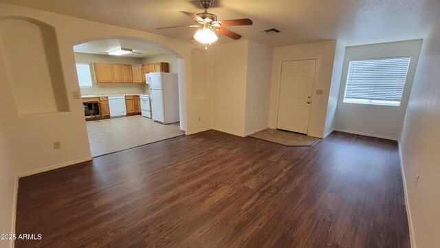unfurnished living room featuring arched walkways, dark wood-style floors, a ceiling fan, and baseboards