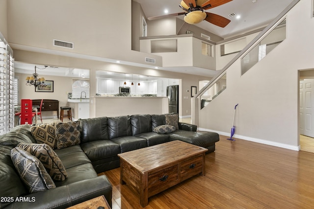 living area with visible vents, wood finished floors, baseboards, ceiling fan with notable chandelier, and a high ceiling