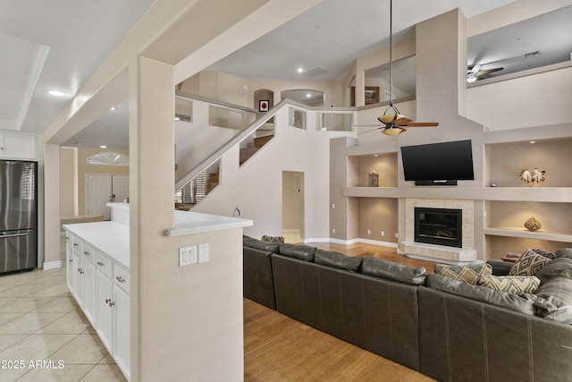 living area featuring stairs, built in shelves, a tiled fireplace, a ceiling fan, and light tile patterned floors