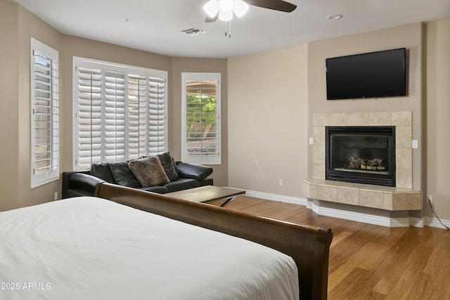 bedroom featuring a tiled fireplace, recessed lighting, baseboards, wood finished floors, and visible vents