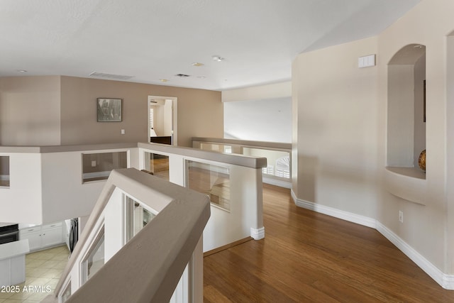 hallway with visible vents, baseboards, light wood-type flooring, arched walkways, and an upstairs landing