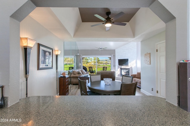 dining space with ceiling fan, a large fireplace, and a raised ceiling