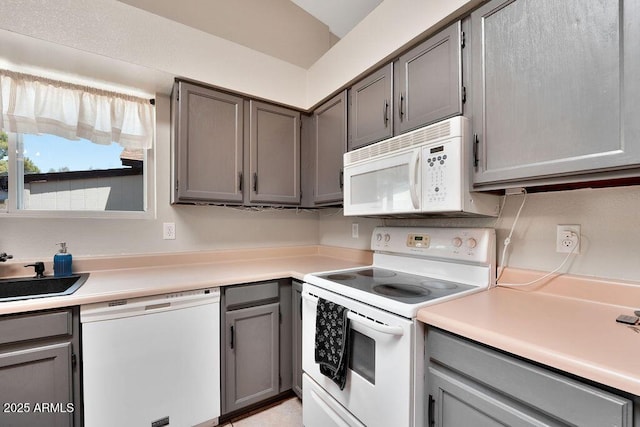 kitchen with gray cabinetry, a sink, white appliances, and light countertops