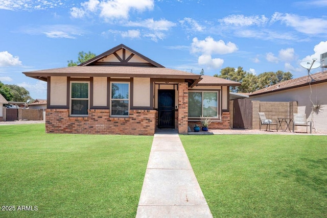view of front facade with fence, a front yard, roof with shingles, and brick siding
