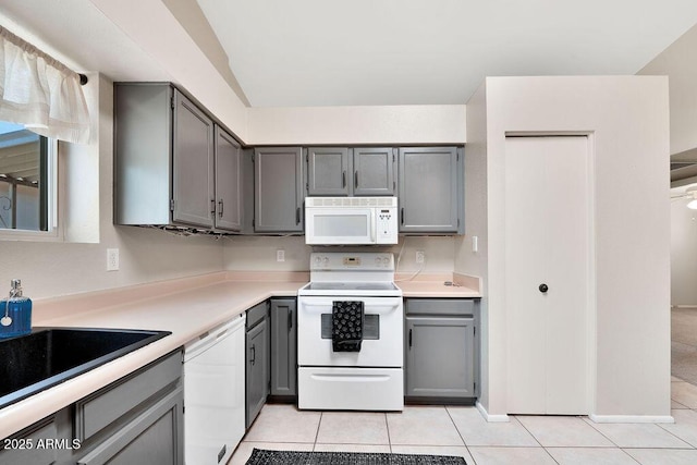 kitchen with gray cabinetry, a sink, light tile patterned flooring, and white appliances