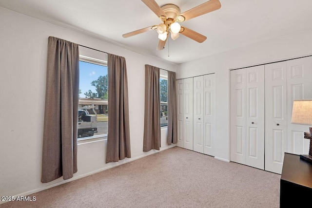 unfurnished bedroom featuring carpet floors, a ceiling fan, baseboards, and multiple closets