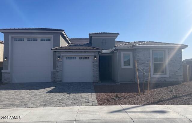 prairie-style home with a garage, decorative driveway, a tiled roof, and stone siding