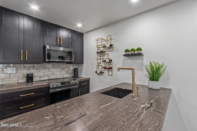 kitchen with stainless steel appliances, a sink, dark stone countertops, decorative backsplash, and recessed lighting