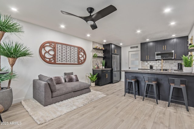 living area featuring bar with sink, recessed lighting, a ceiling fan, light wood-type flooring, and baseboards