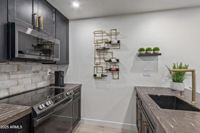 kitchen with black electric range oven, stainless steel microwave, dark stone counters, baseboards, and light wood-style flooring