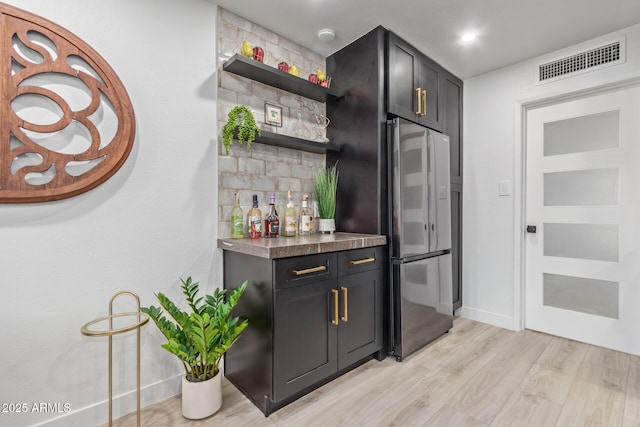 indoor dry bar with freestanding refrigerator, light wood-style flooring, and baseboards