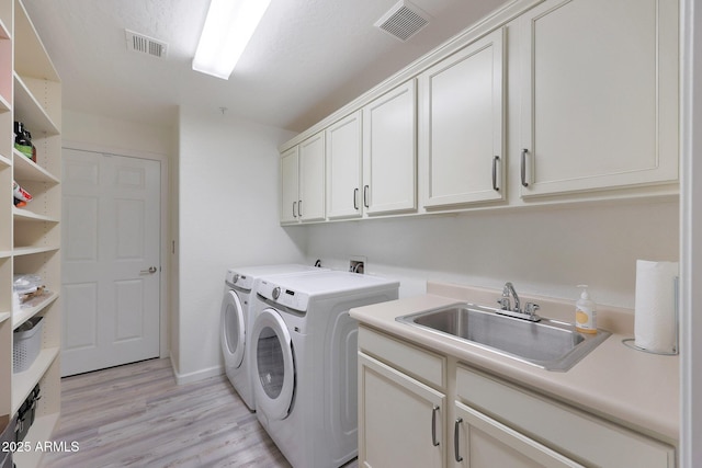 washroom featuring cabinets, washing machine and dryer, sink, and light hardwood / wood-style floors