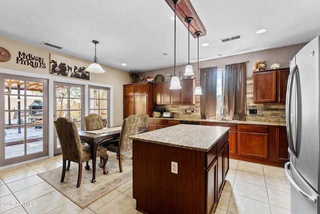 kitchen with pendant lighting, stainless steel refrigerator, a center island, light stone countertops, and a healthy amount of sunlight