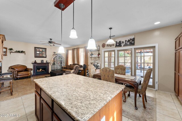 kitchen with light tile patterned floors, ceiling fan, hanging light fixtures, light stone counters, and a kitchen island