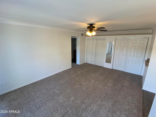 unfurnished bedroom featuring ceiling fan, crown molding, dark carpet, and two closets