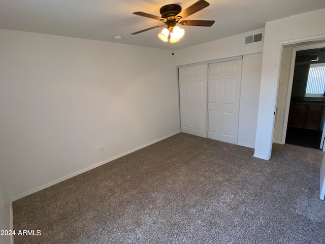 unfurnished bedroom with ceiling fan, a closet, and dark colored carpet