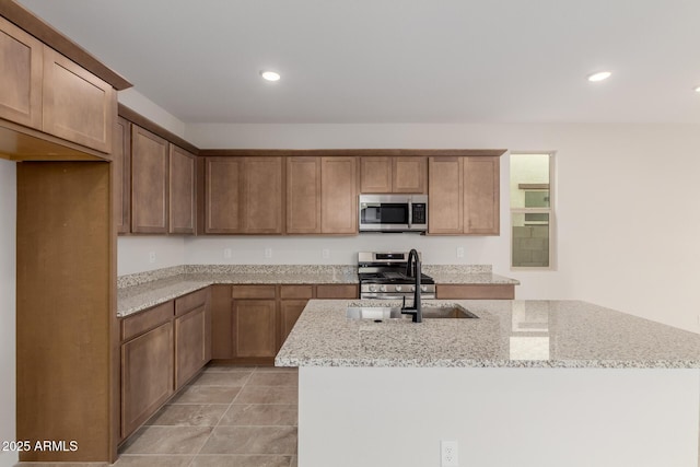 kitchen featuring an island with sink, appliances with stainless steel finishes, light stone counters, a sink, and recessed lighting