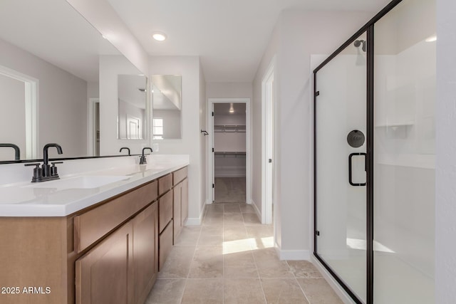 full bathroom featuring double vanity, a stall shower, a sink, and a walk in closet