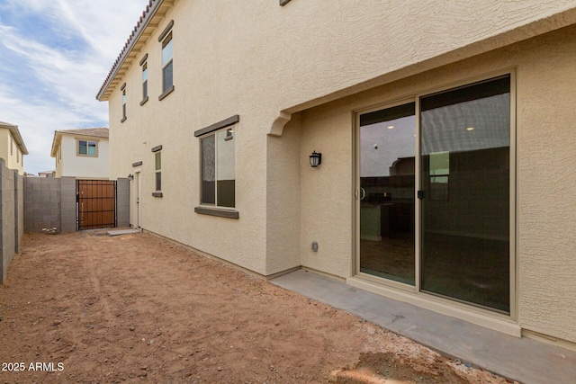 rear view of property featuring fence, a gate, and stucco siding