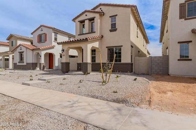 mediterranean / spanish-style home featuring a tile roof, fence, and stucco siding