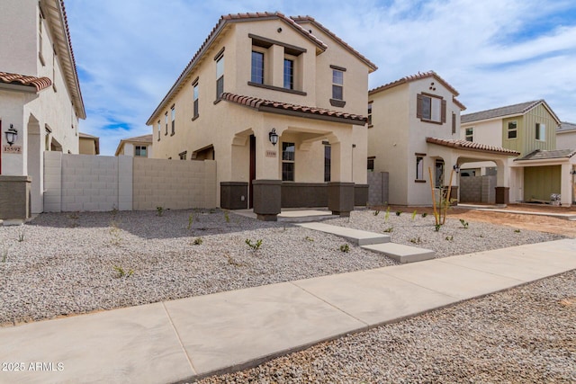 mediterranean / spanish house featuring a tile roof, fence, and stucco siding