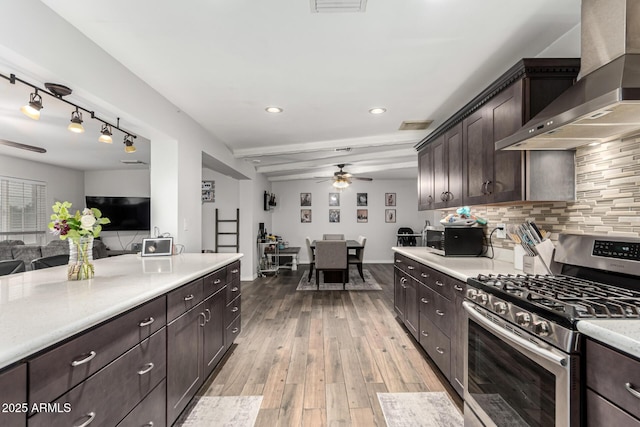 kitchen with light countertops, backsplash, stainless steel gas range, light wood-type flooring, and wall chimney exhaust hood