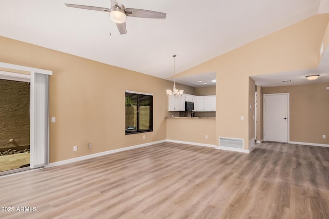 unfurnished living room with visible vents, ceiling fan with notable chandelier, light wood-style floors, baseboards, and vaulted ceiling