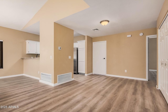 unfurnished living room featuring light wood-type flooring, visible vents, and baseboards