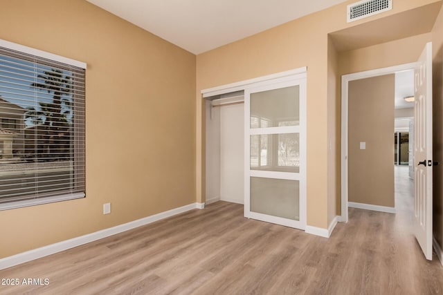 unfurnished bedroom featuring visible vents, baseboards, a closet, and wood finished floors