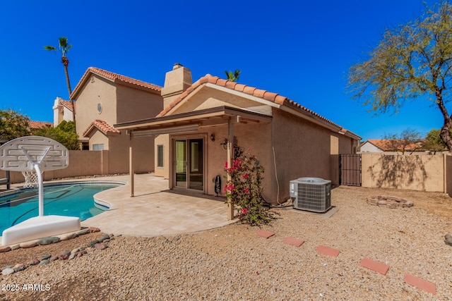 back of house with stucco siding, cooling unit, a chimney, a fenced backyard, and a patio