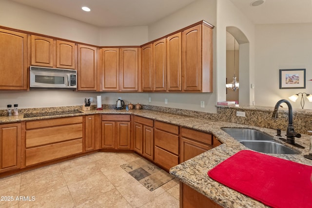 kitchen featuring sink, light stone countertops, hanging light fixtures, and black electric stovetop