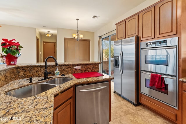 kitchen featuring sink, an inviting chandelier, pendant lighting, stainless steel appliances, and light stone countertops