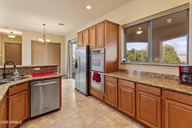 kitchen with sink, appliances with stainless steel finishes, hanging light fixtures, light stone counters, and a notable chandelier