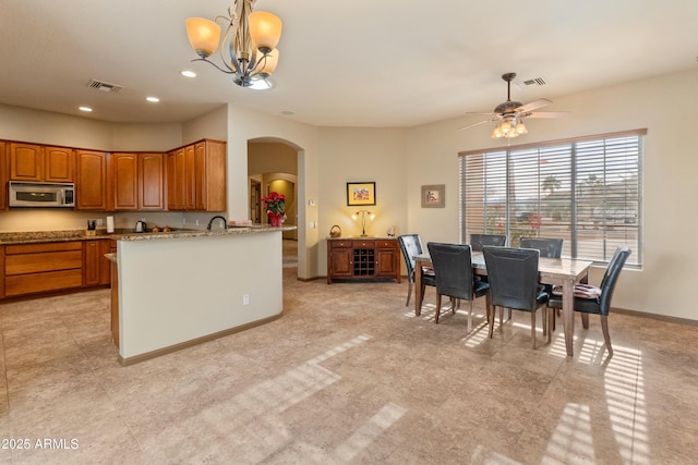 kitchen featuring sink, ceiling fan with notable chandelier, light stone counters, and decorative light fixtures