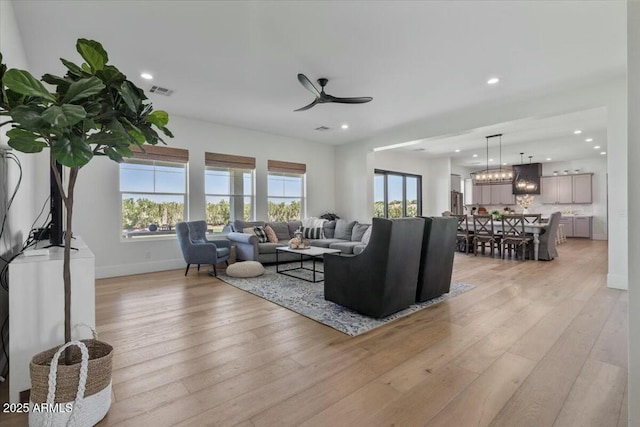 living room with ceiling fan, light wood-type flooring, baseboards, recessed lighting, and a chandelier