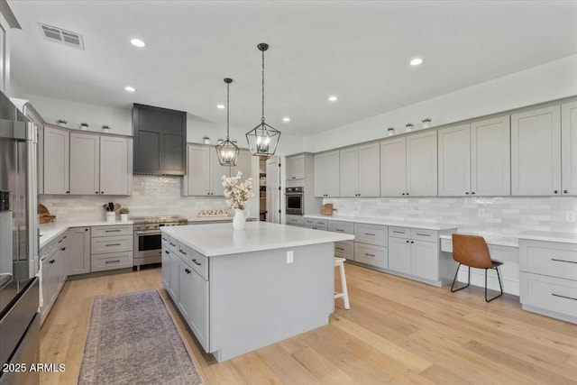 kitchen with gray cabinets, high end appliances, a kitchen island, decorative backsplash, and a kitchen bar