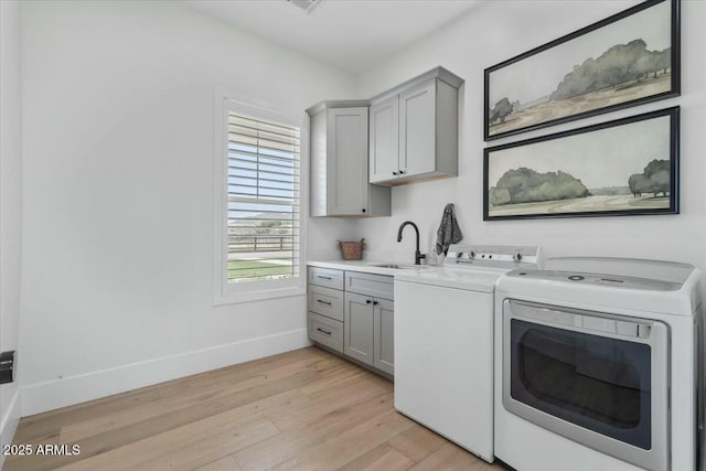 laundry room with cabinet space, washing machine and clothes dryer, baseboards, and light wood-style flooring