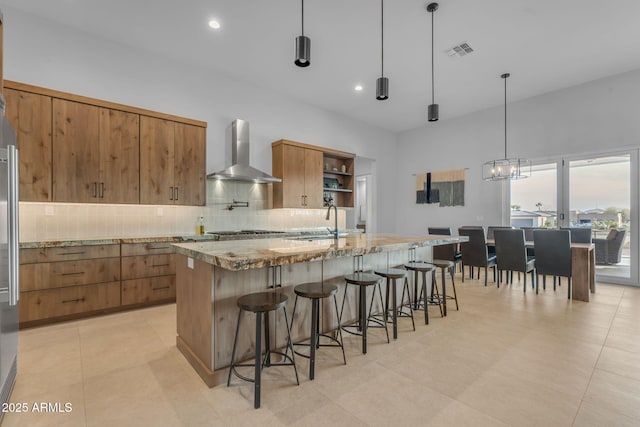 kitchen featuring wall chimney range hood, brown cabinetry, visible vents, and tasteful backsplash